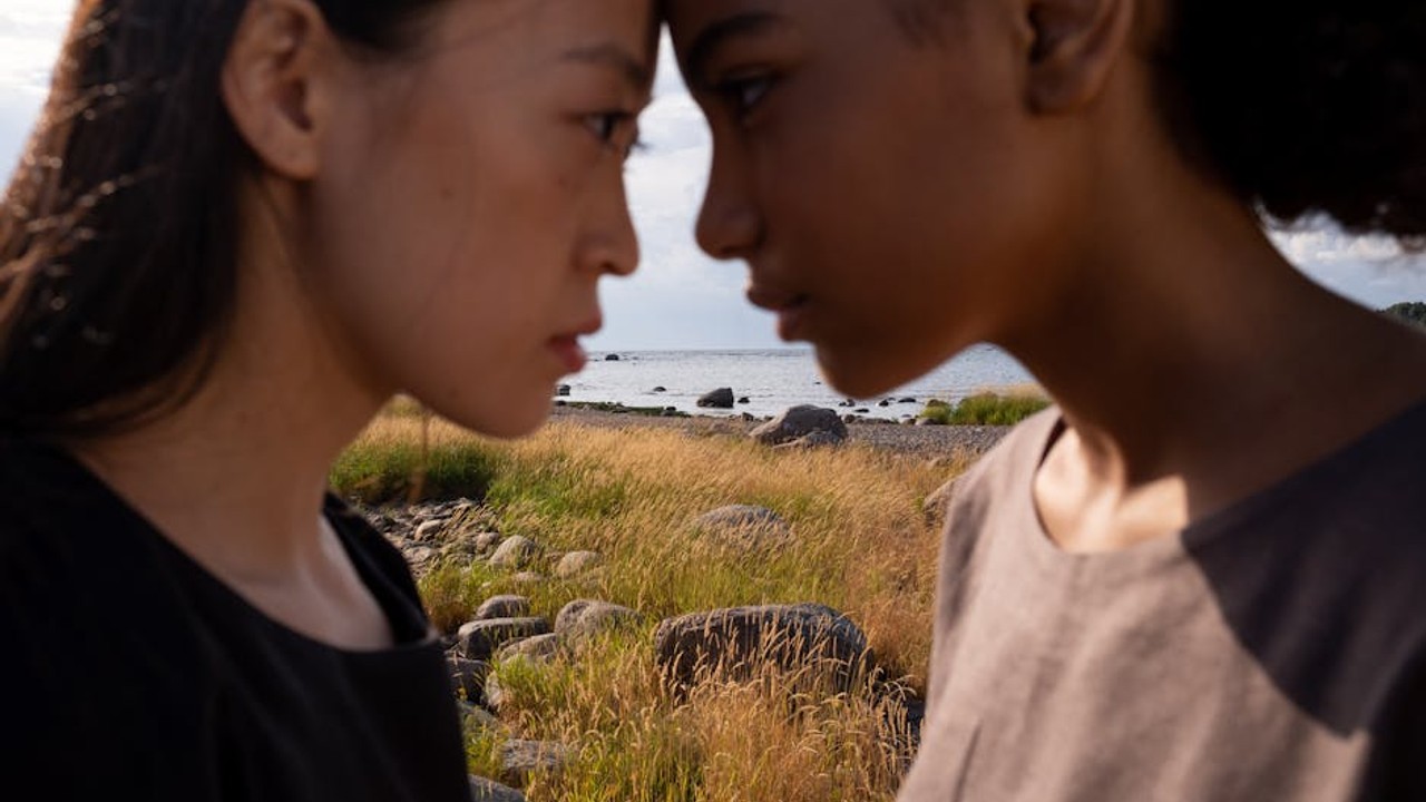 A team of esports players in a gaming house, attentively listening to their coach who is pointing at a projector screen displaying tactical maps for both CS2 and Valorant.